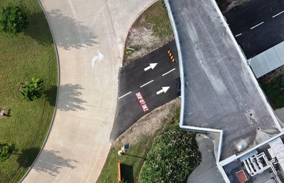 Spexi drone capture of the same drop-off lane: lane arrows, the painted DROP OFF ONLY text, a speed bump, rooftop equipment and individual shrubs are distinct.