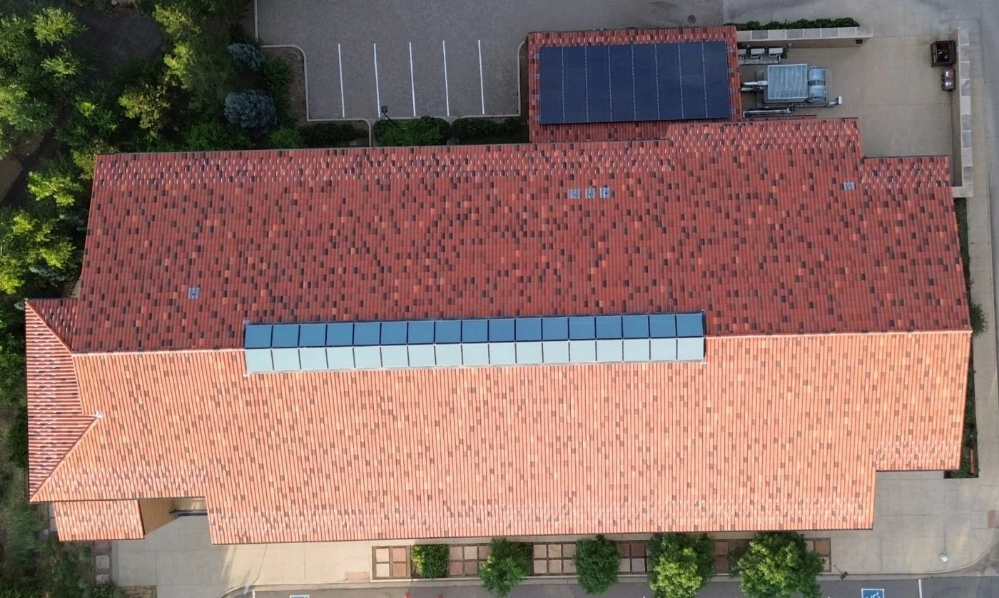 Nadir capture looking straight down on the building roof: red clay tiles, the skylight strip, roof vents, the solar array and rooftop mechanical units.