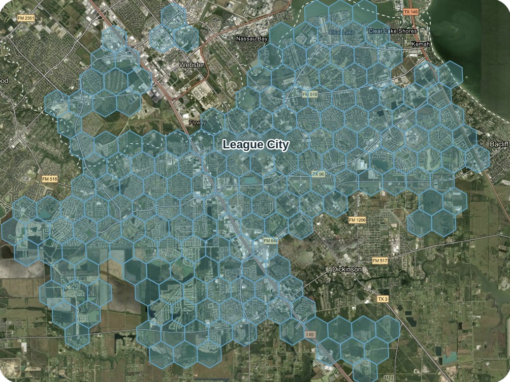 Satellite map of League City, Texas, between Webster, Clear Lake, Dickinson and Galveston Bay, covered by a grid of translucent blue Spexigon hexagons showing the area with Living Coverage.