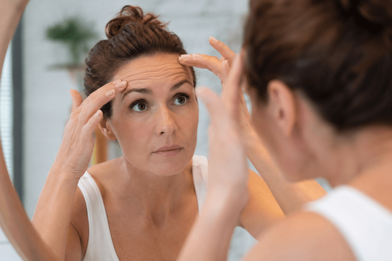 Woman examining forehead wrinkles in mirror before Dysport treatment in Hingham Massachusetts