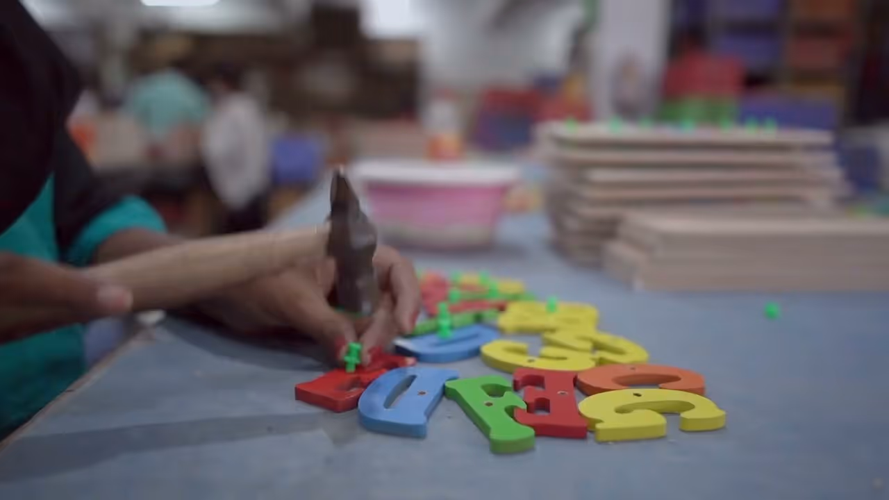 Person hammering green pegs into colorful wooden alphabet letters on a table.