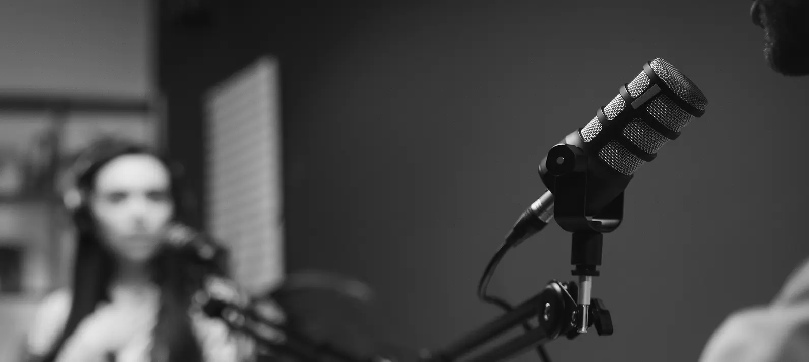 Podcast mics setup with woman in background and chin of man.