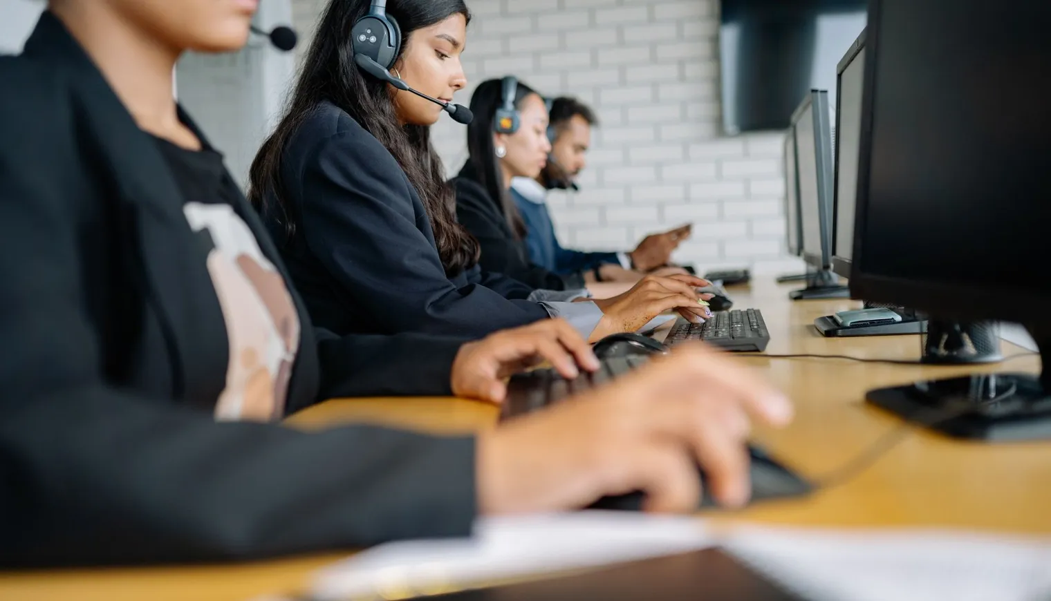 Four call center agents with headsets working on computers in an office setting.