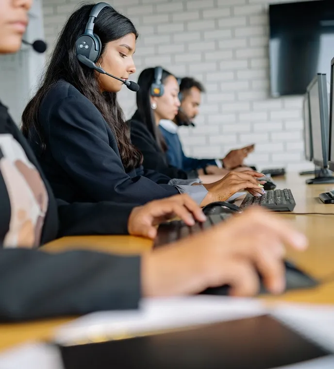 Row of call center agents with headsets typing on keyboards at a long desk.