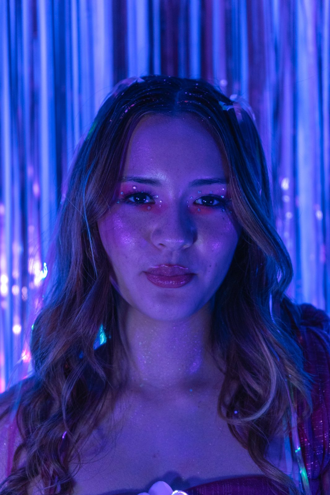 Studio portrait against a foil tinsel backdrop under violet light