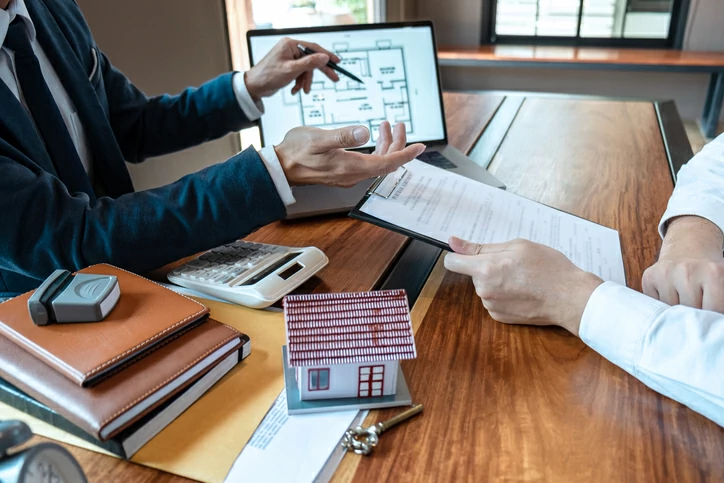professionnels en train de pointer l'écran d'un ordinateur portable avec un stylo devant une autre personne tenant un document à la main