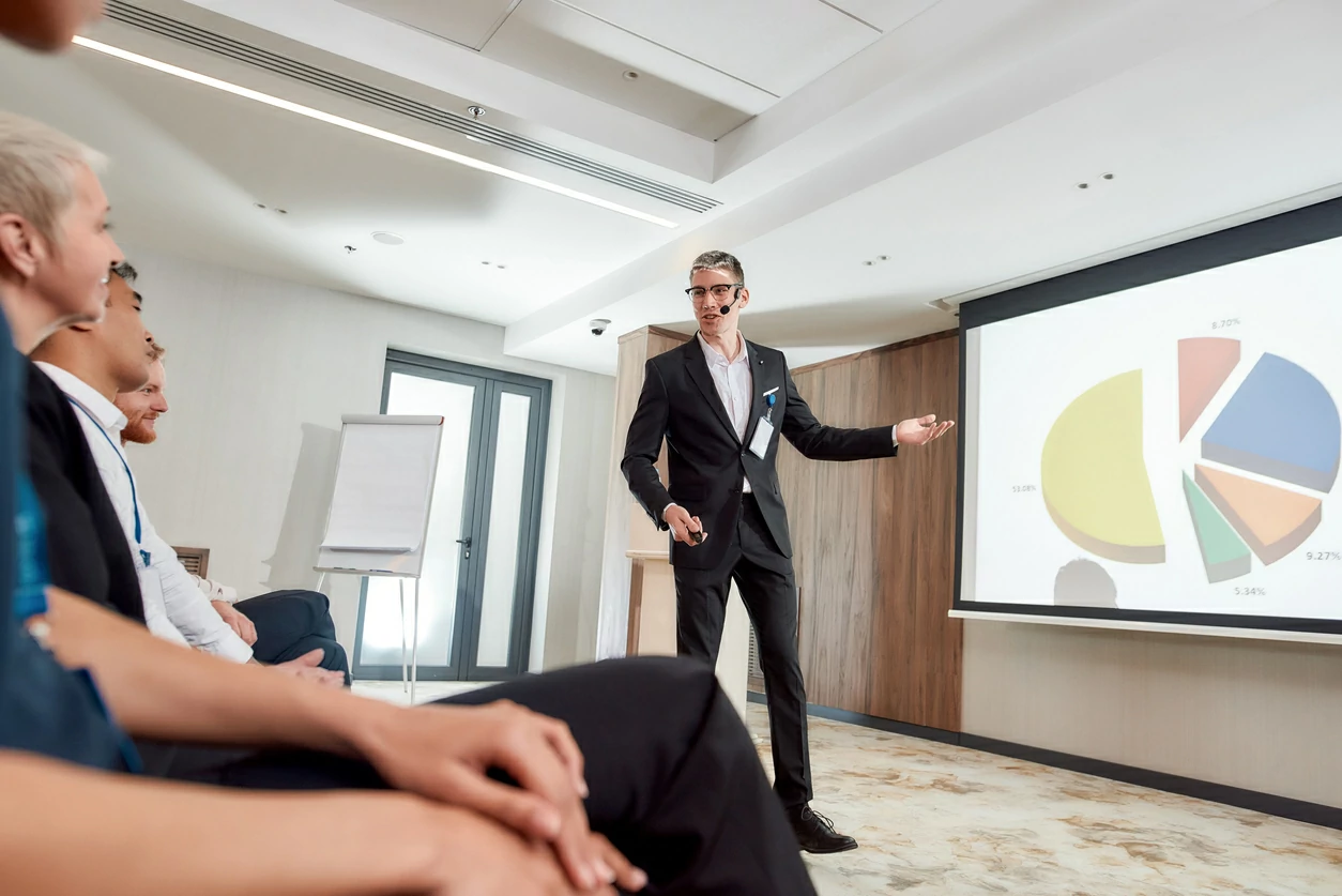 Homme en costume en pleine présentation devant un tableau blanc.