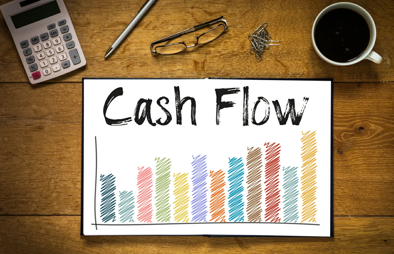 Document ouvert avec des graphiques et le mot cash-flow, tasse de café, calculatrice, lunettes, stylo et des trombones.