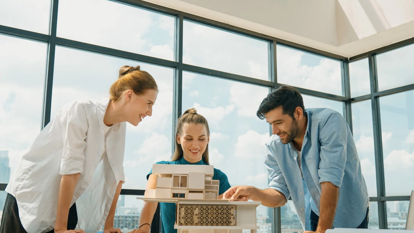 Deux femmes et un homme regardant une maquette de maison.