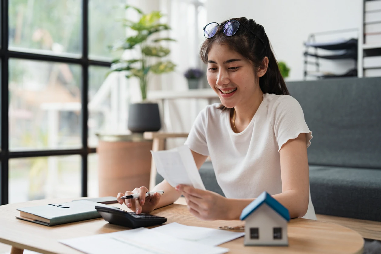 Jeune femme asiatique souriante qui utilise une calculatrice et tenant un papier dans la main.