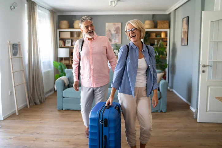 Un couple d'une cinquantaine d'année portant une valise dans une pièces meublées.