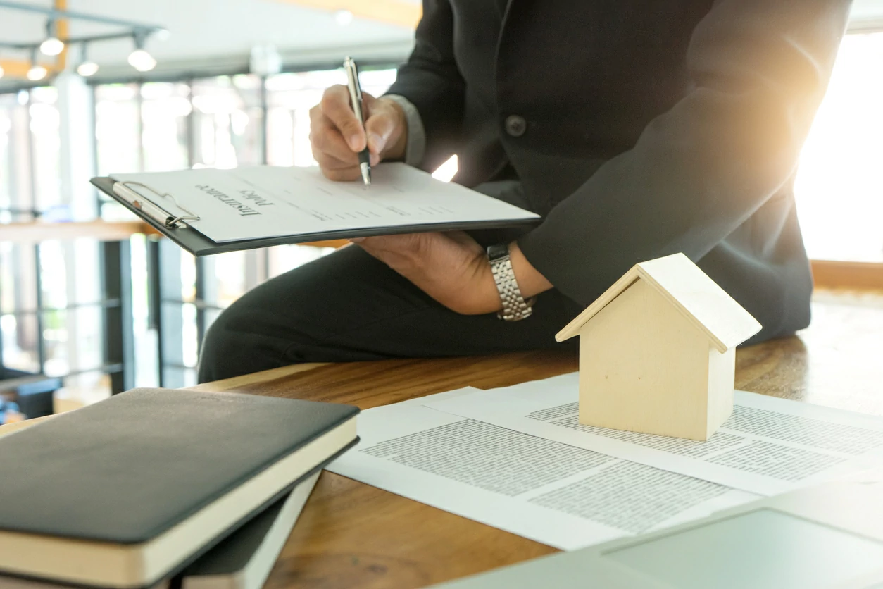Homme en train de signer un contrat avec une petite maison en bois posée sur la table.