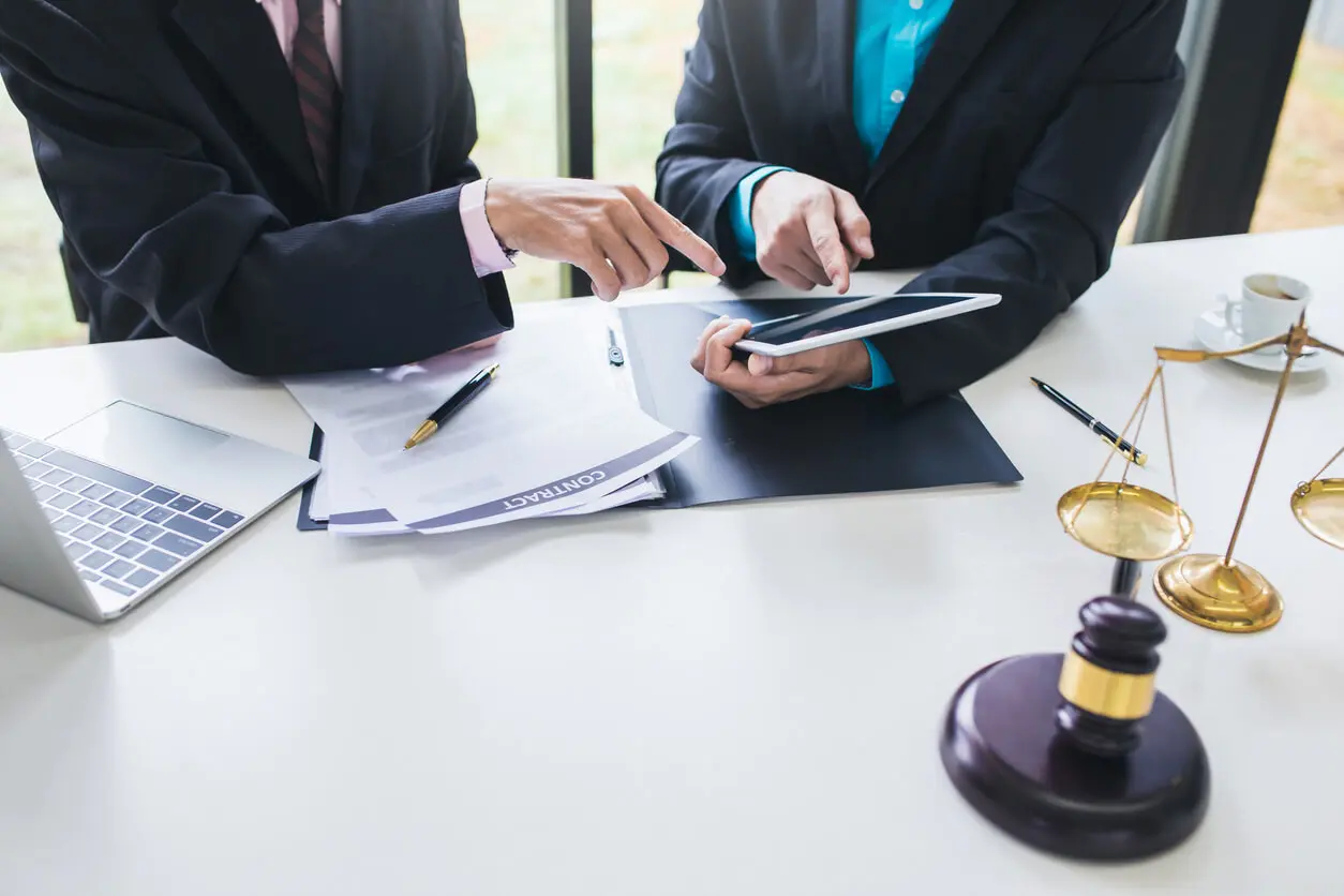 Professionnel juridique tenant une tablette à côté d'un homme et des documents divers.