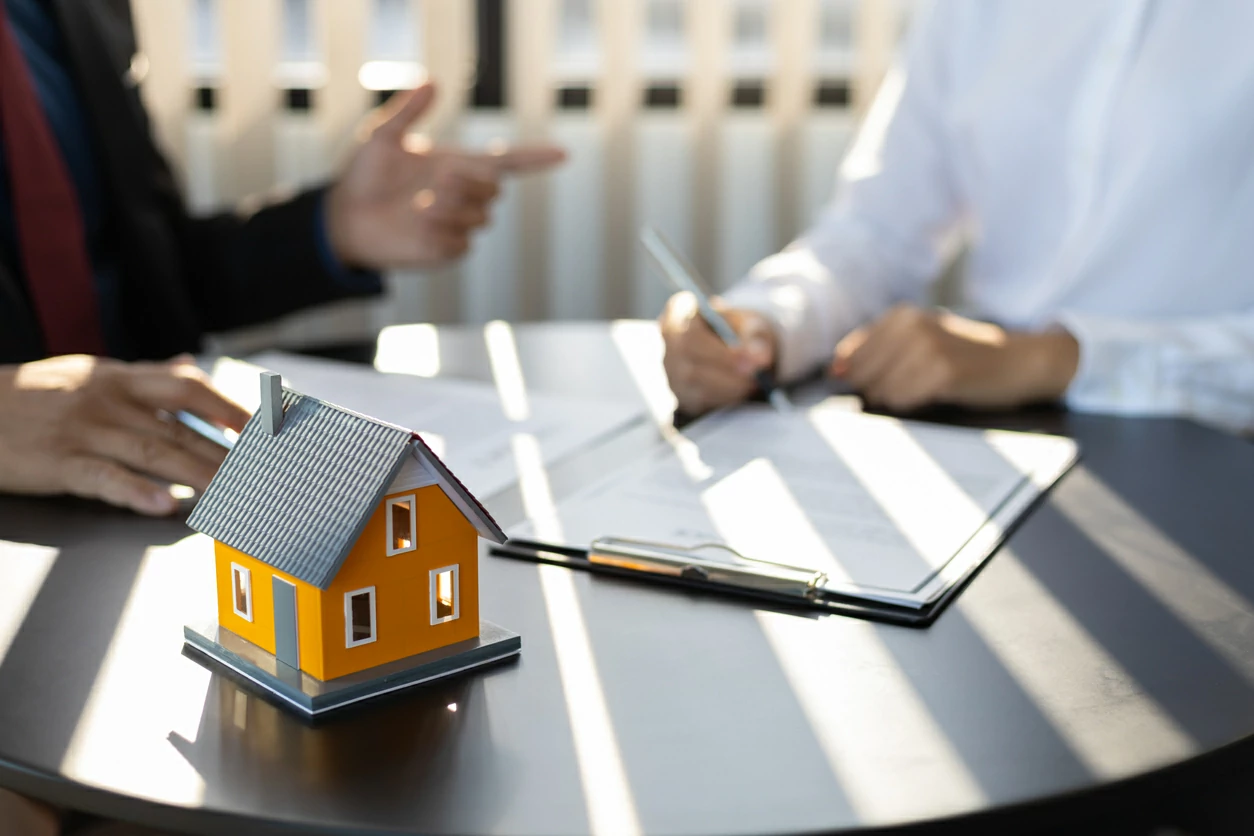 Maquette de maison et deux personnes dont l'une signant un document en arrière-plan.
