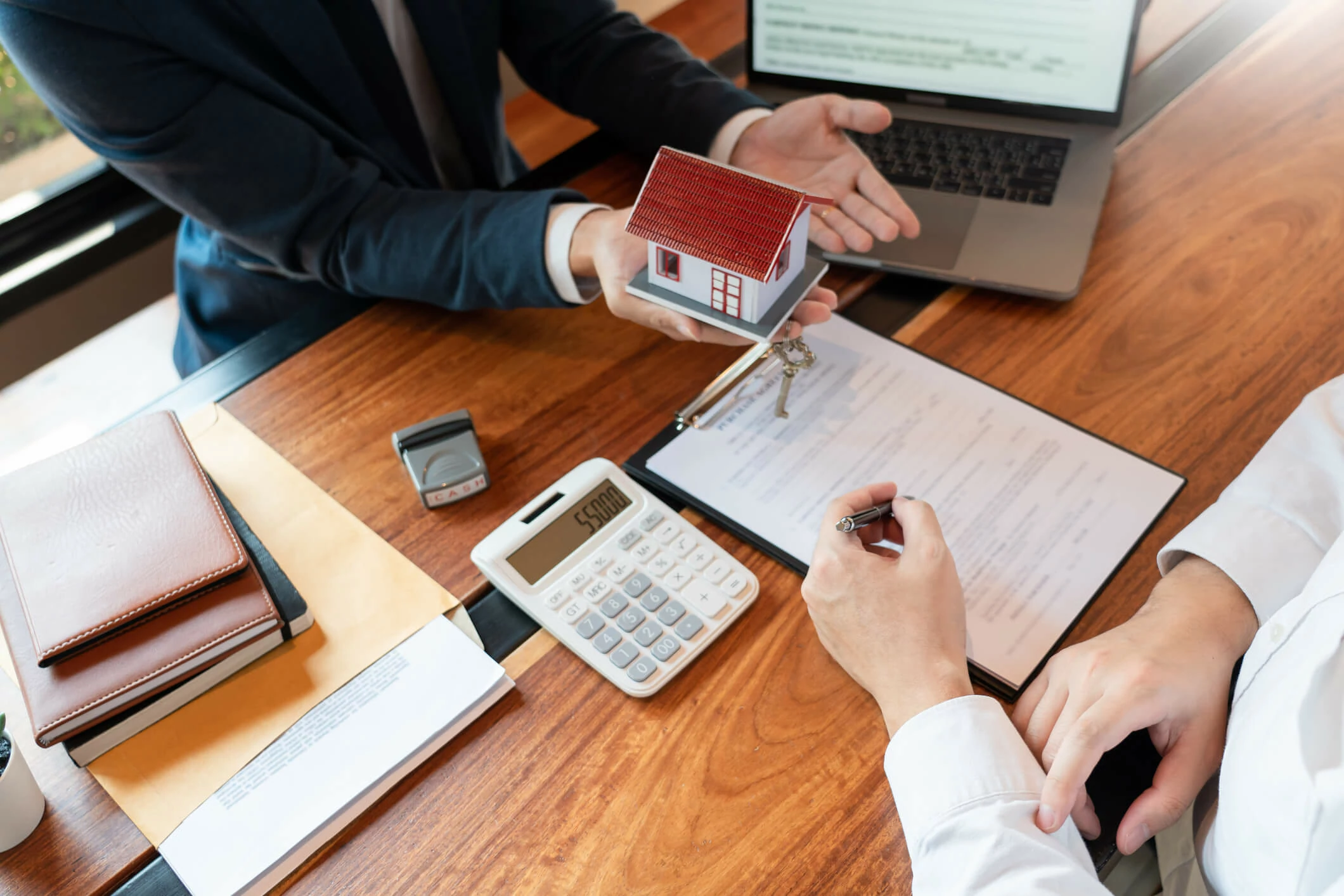 Homme tenant une petite maison et une clé de maison devant un homme qui s'apprêt à signer un document.