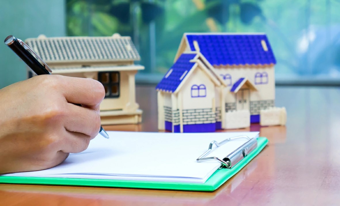 Main qui signe un document à coté de deux petites maisons