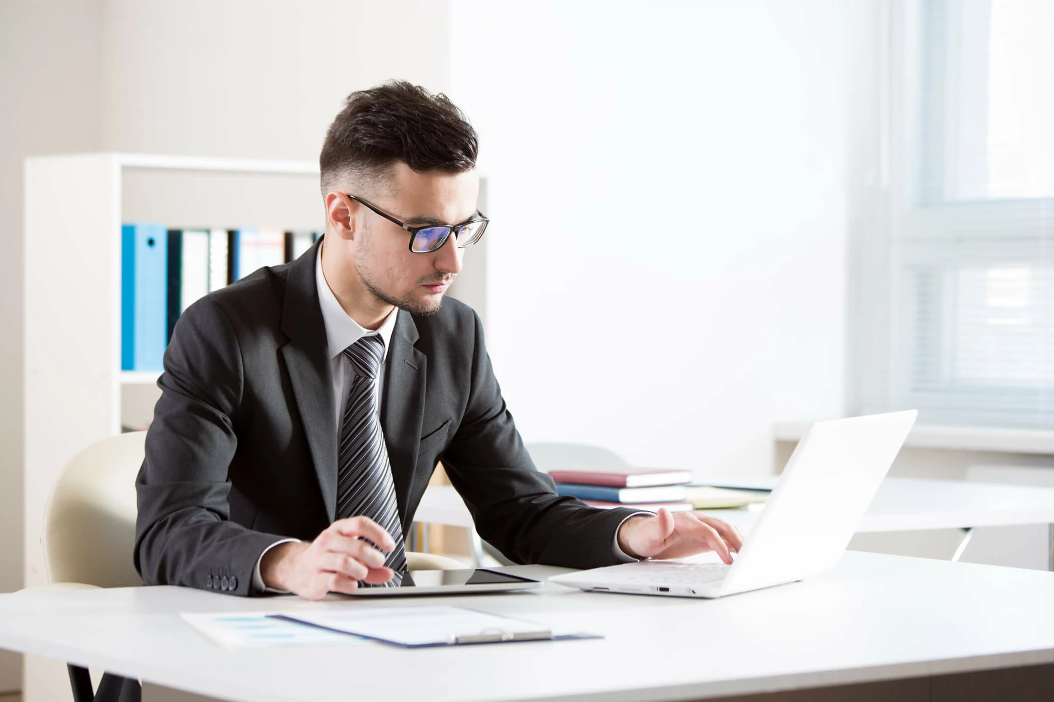 Homme concentré devant un ordinateur portable, une tablette et des documents.