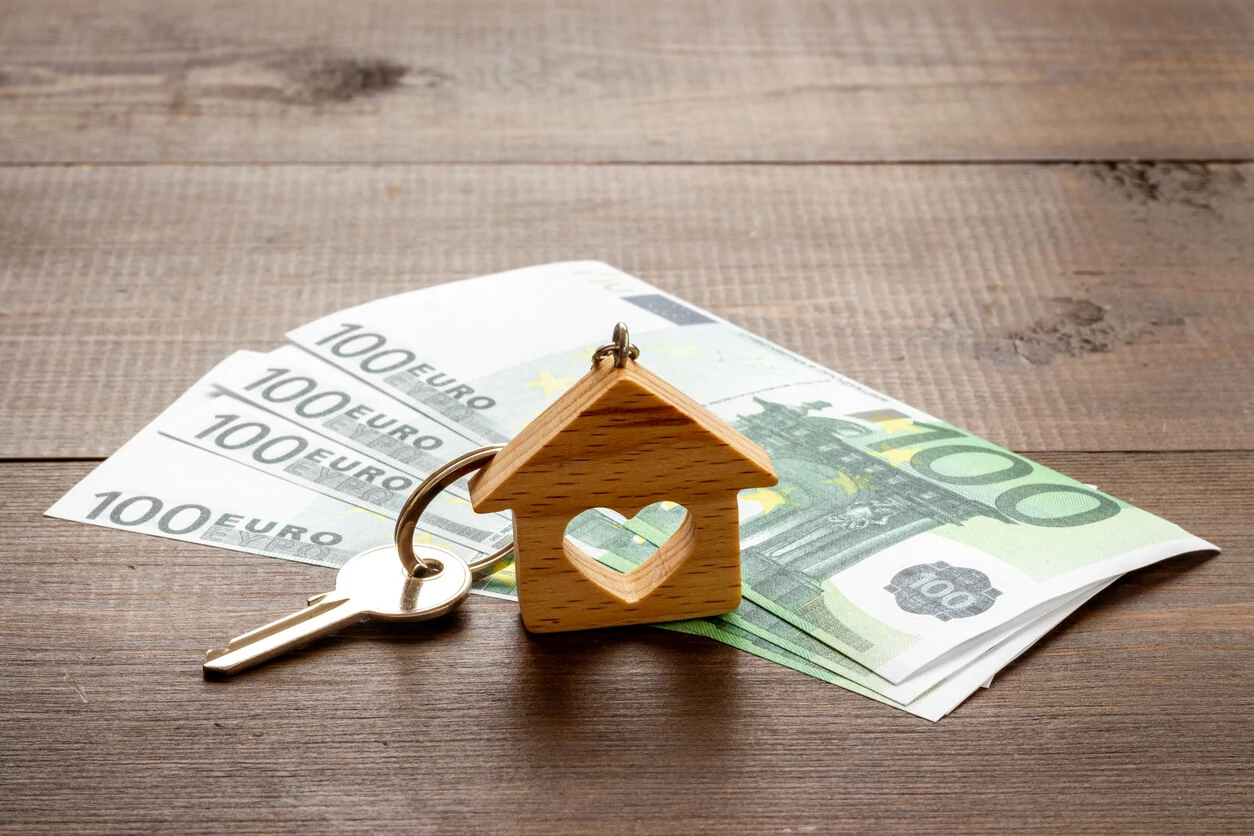 Clé et porte-clé en forme de maison posés au-dessus de plusieurs billets de 100 euros.