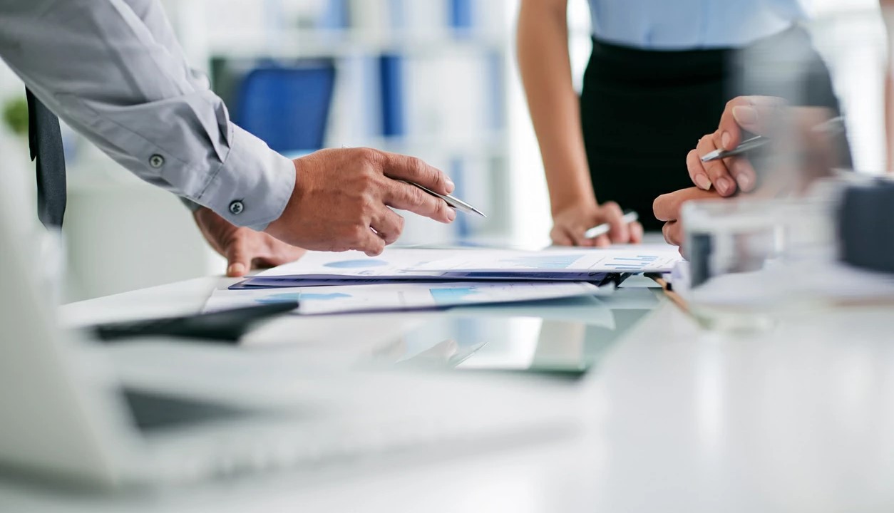Trois personnes avec stylo à la main analysant des documents divers.