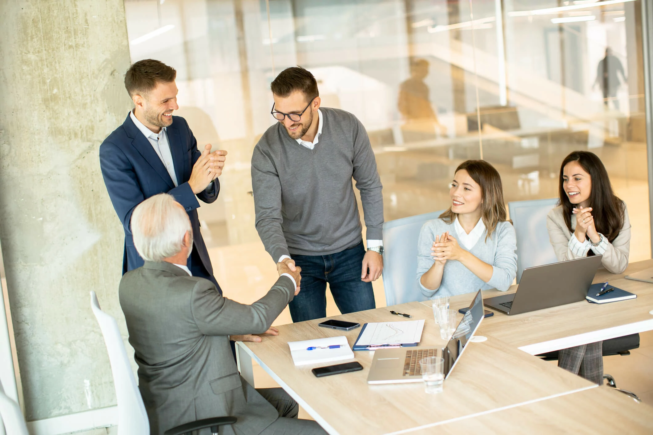 Homme serrant la main d'un homme plus âgé et trois personnes qui applaudissent.