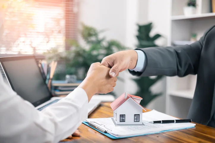 Homme et femme se serrant la main au-dessus d'un document et d'une petite maison.