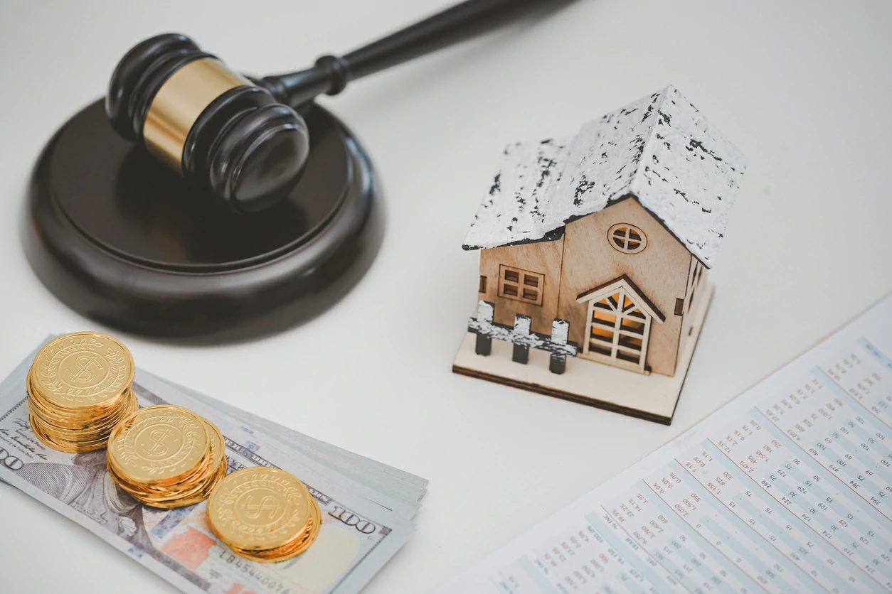 Marteau de jugement, maquette de maison, billet en dollars et pièces de monnaie.s