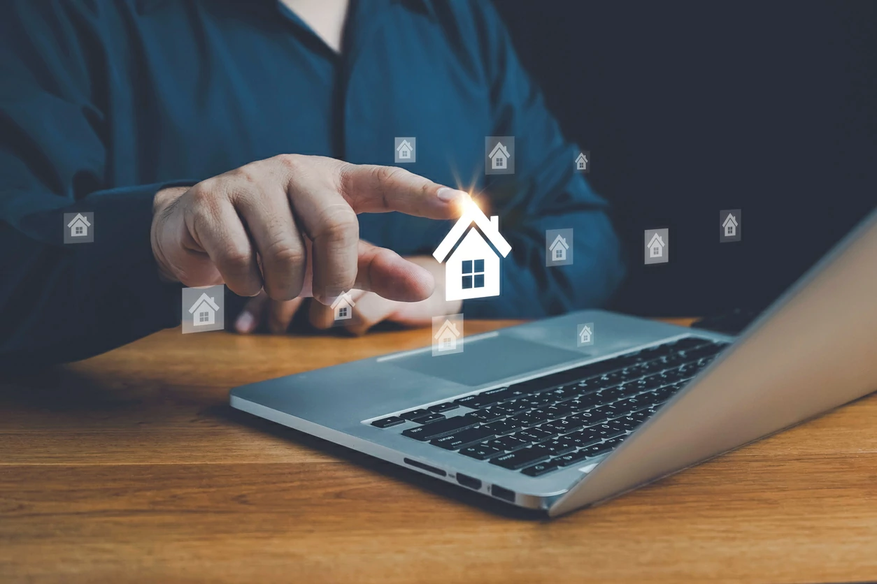 Main d'un homme pointant sur un hologramme d'une maison au-dessus d'un ordinateur portable.