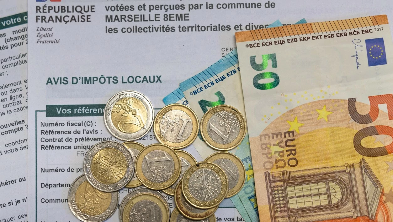 Documents d'impôts, pièces et billets d'argent posés par dessus.