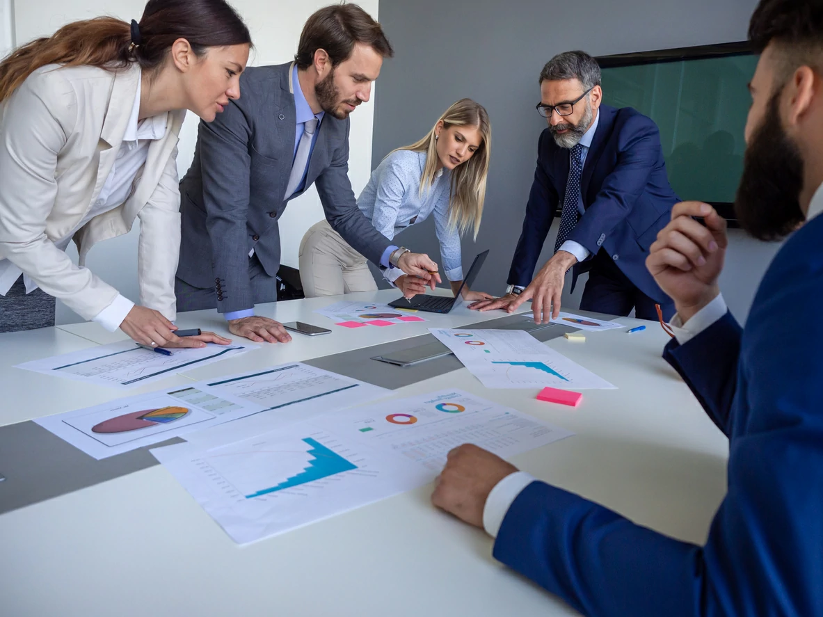 5 professionnels en train de consulter des documents autour d'une tableau.