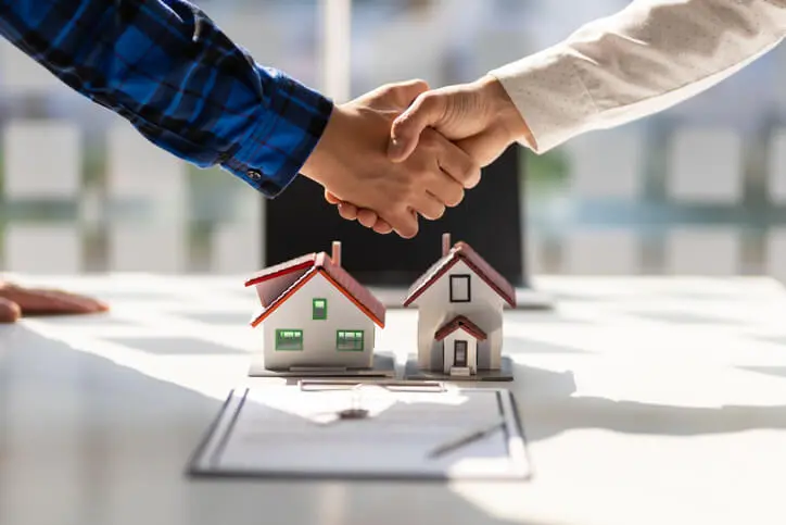 Deux hommes se serrant la main au-dessus de documents et de deux petites maisons.