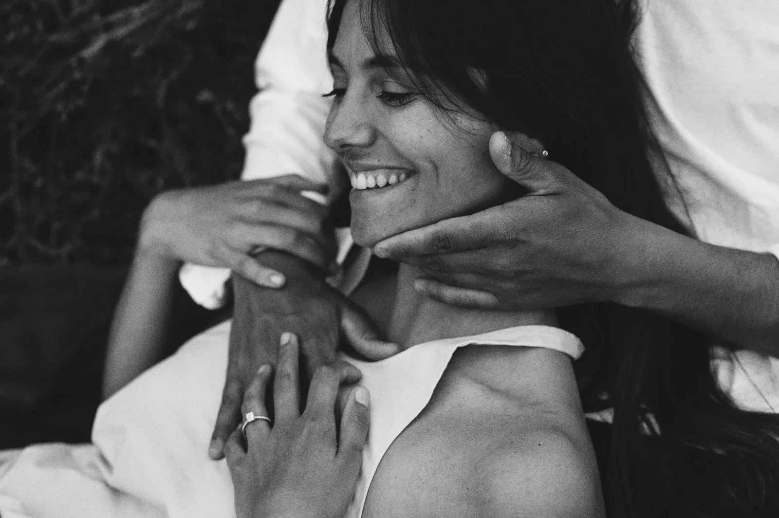 Servizio di coppia in bianco e nero: lei sorride mentre lui le sfiora il collo con le mani