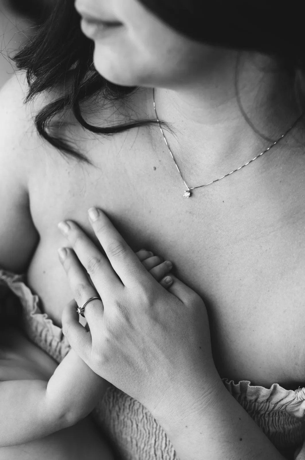 Dettaglio mom & me in bianco e nero: la mano del bebè appoggiata sul petto della mamma