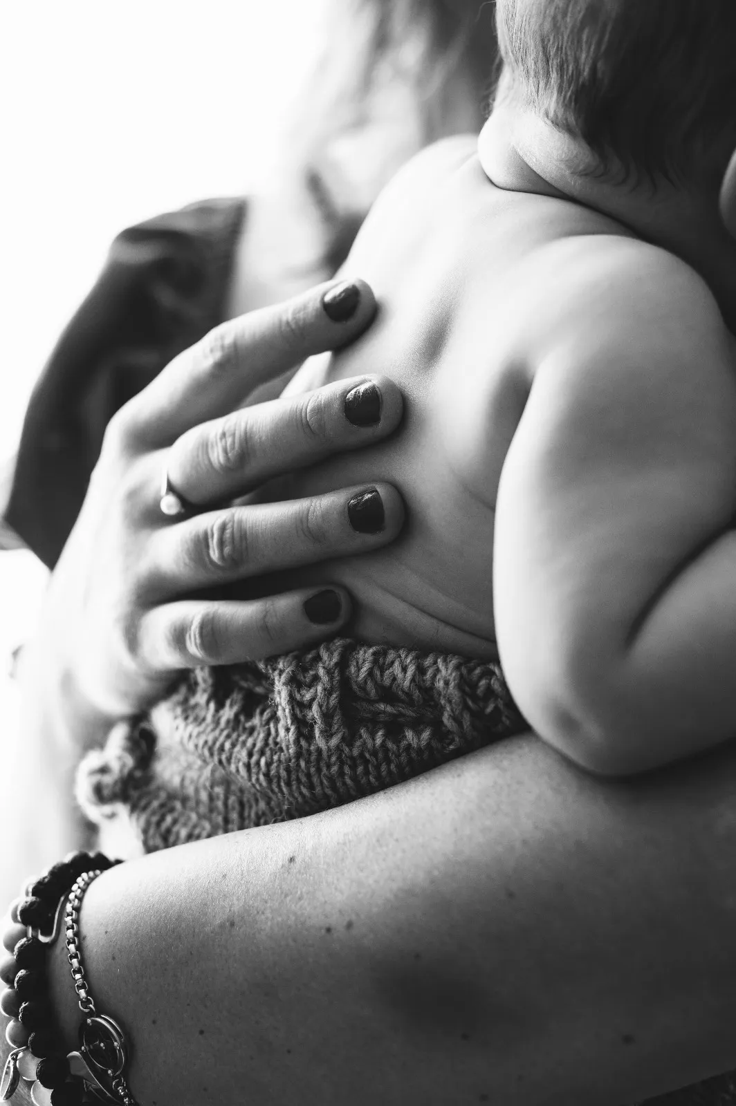 Dettaglio mom & me in bianco e nero: il bebè in braccio con la mano della mamma sulla schiena