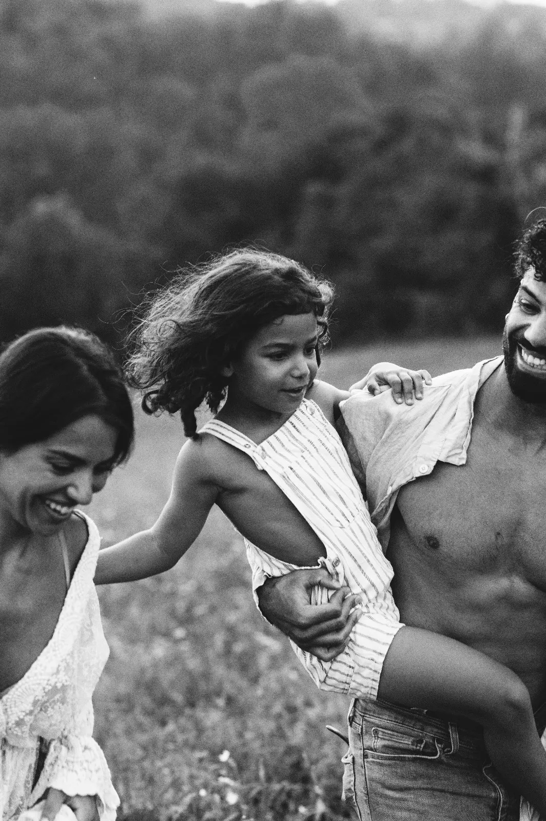 Servizio di famiglia in bianco e nero: mamma e papà che ridono con la figlia in braccio in un campo