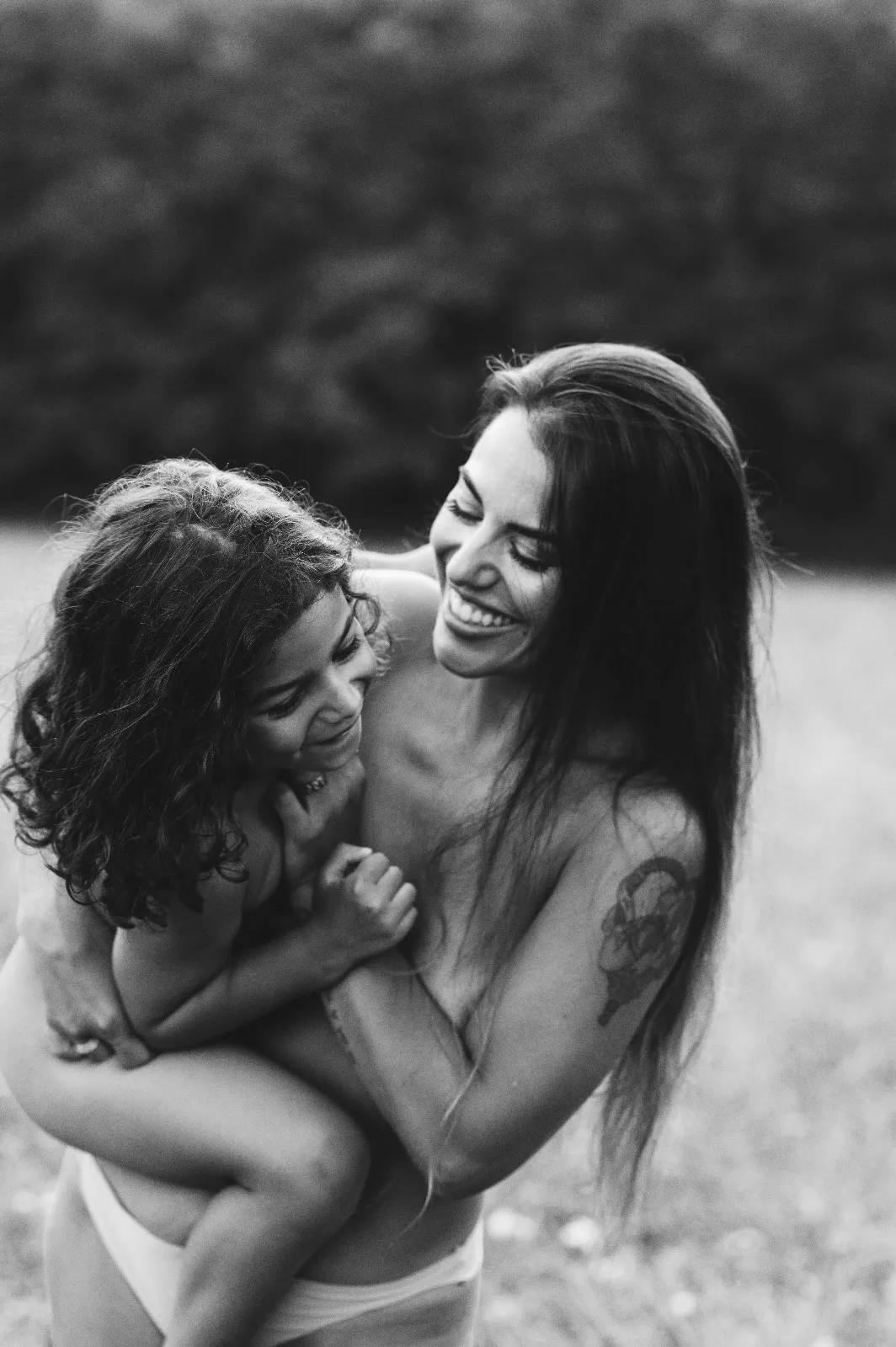 Sessione di famiglia in bianco e nero: mamma che ride con la figlia in braccio in un campo