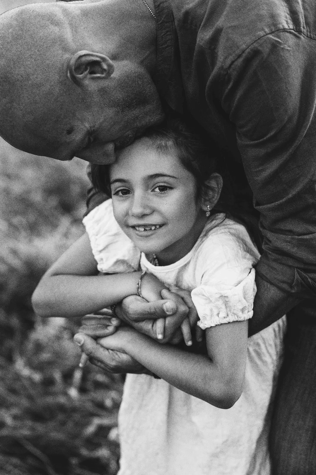 Servizio di famiglia in bianco e nero: papà che bacia la testa della figlia tenendole le mani