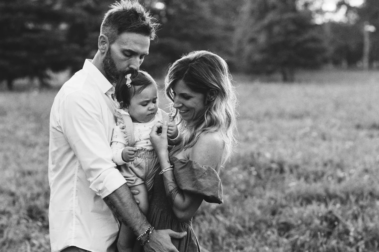 Sessione primo compleanno in bianco e nero: mamma e papà con la bimba in braccio in un prato