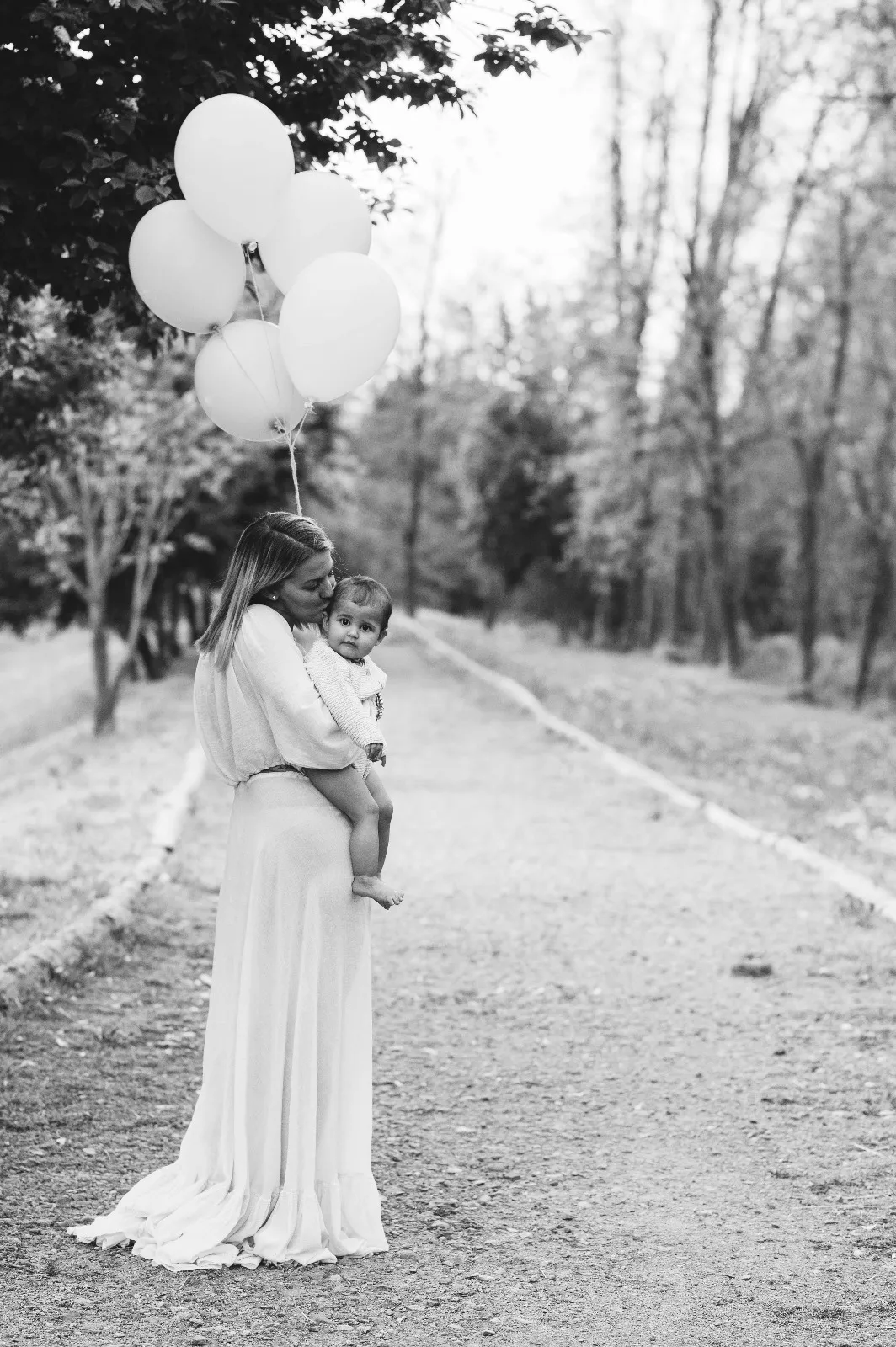 Servizio fotografico primo compleanno in esterna: mamma con la bimba in braccio e i palloncini, in bianco e nero
