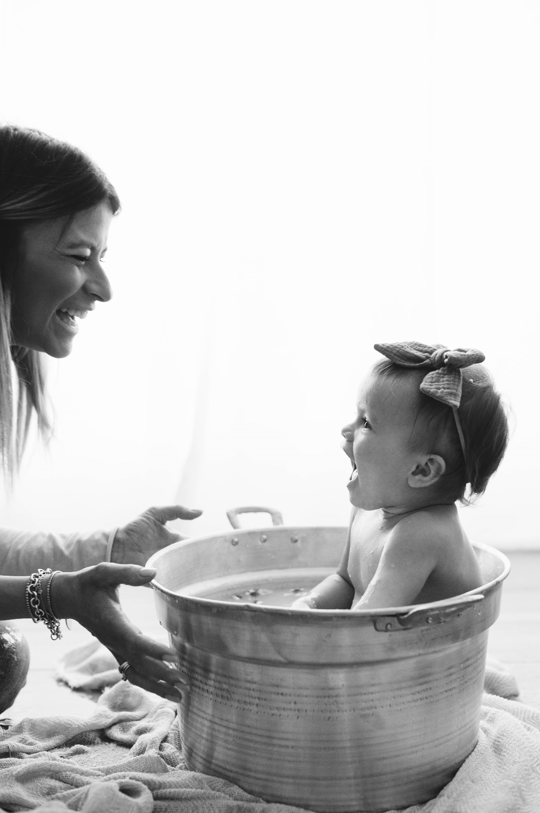 Sessione smash cake in bianco e nero: la bimba nella tinozza dopo la torta, con la mamma che ride accanto