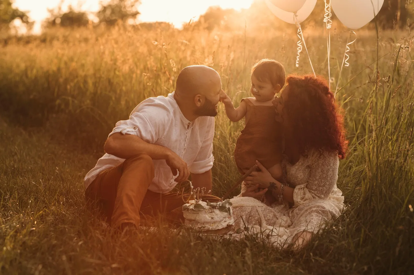 Servizio fotografico smash cake al tramonto: mamma e papà seduti nel prato con la bimba e la torta