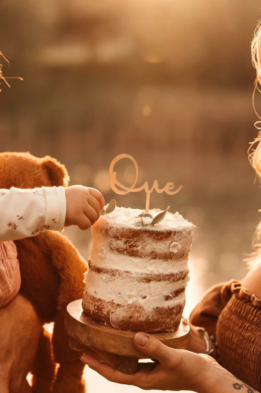 Sessione smash cake al tramonto: la torta con la scritta One offerta al bimbo che allunga la mano