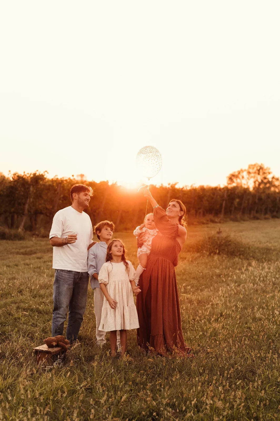 Servizio fotografico primo compleanno al tramonto: famiglia di cinque persone in un campo, con il palloncino verso il sole