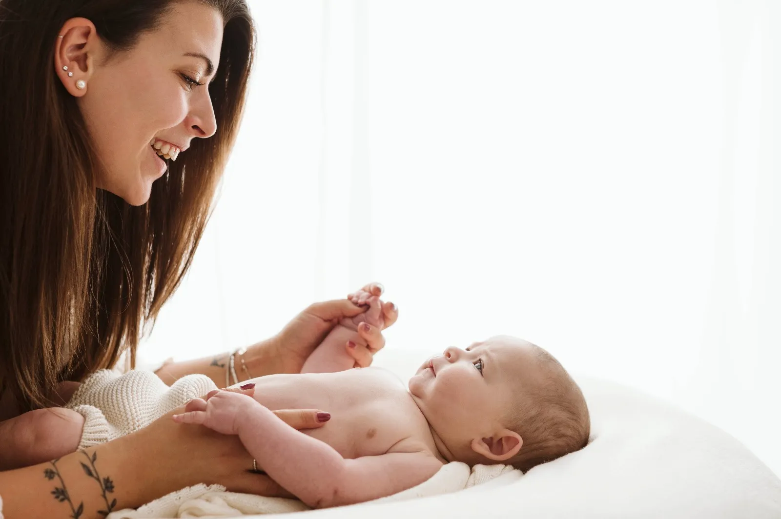 Sessione mamma e figlio: la mamma sorride al bebè disteso, tenendogli le mani