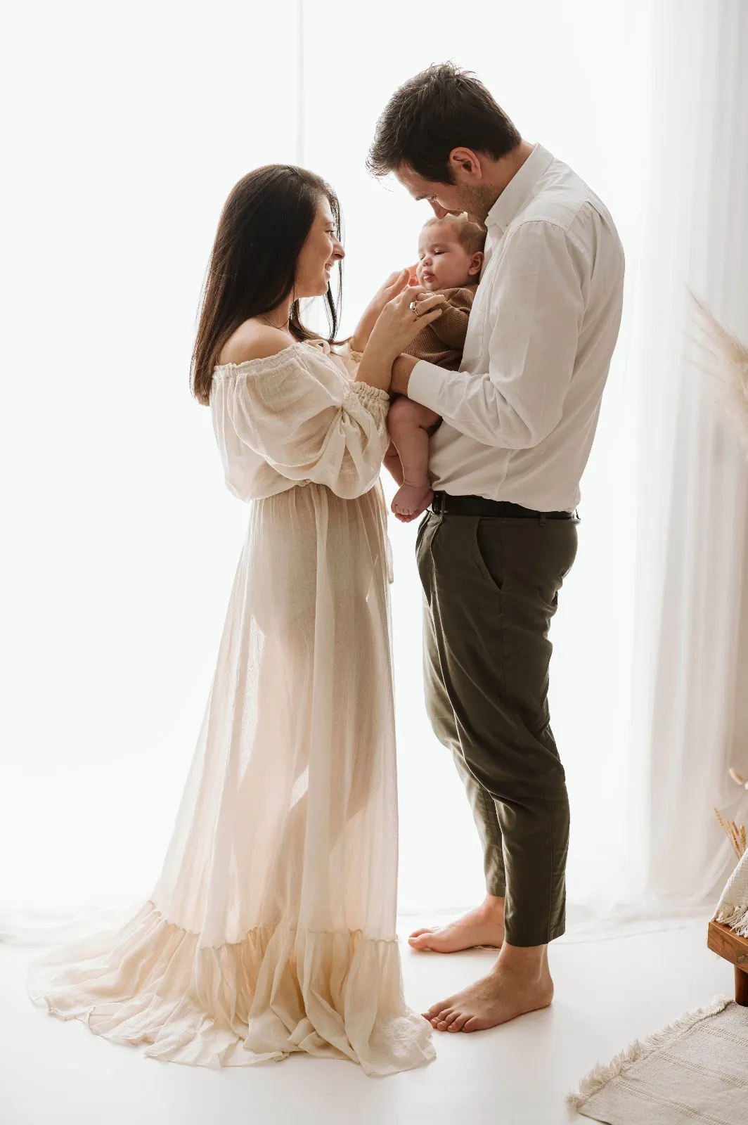 Servizio fotografico bebè in studio: mamma e papà in piedi con il bimbo in braccio, luce naturale