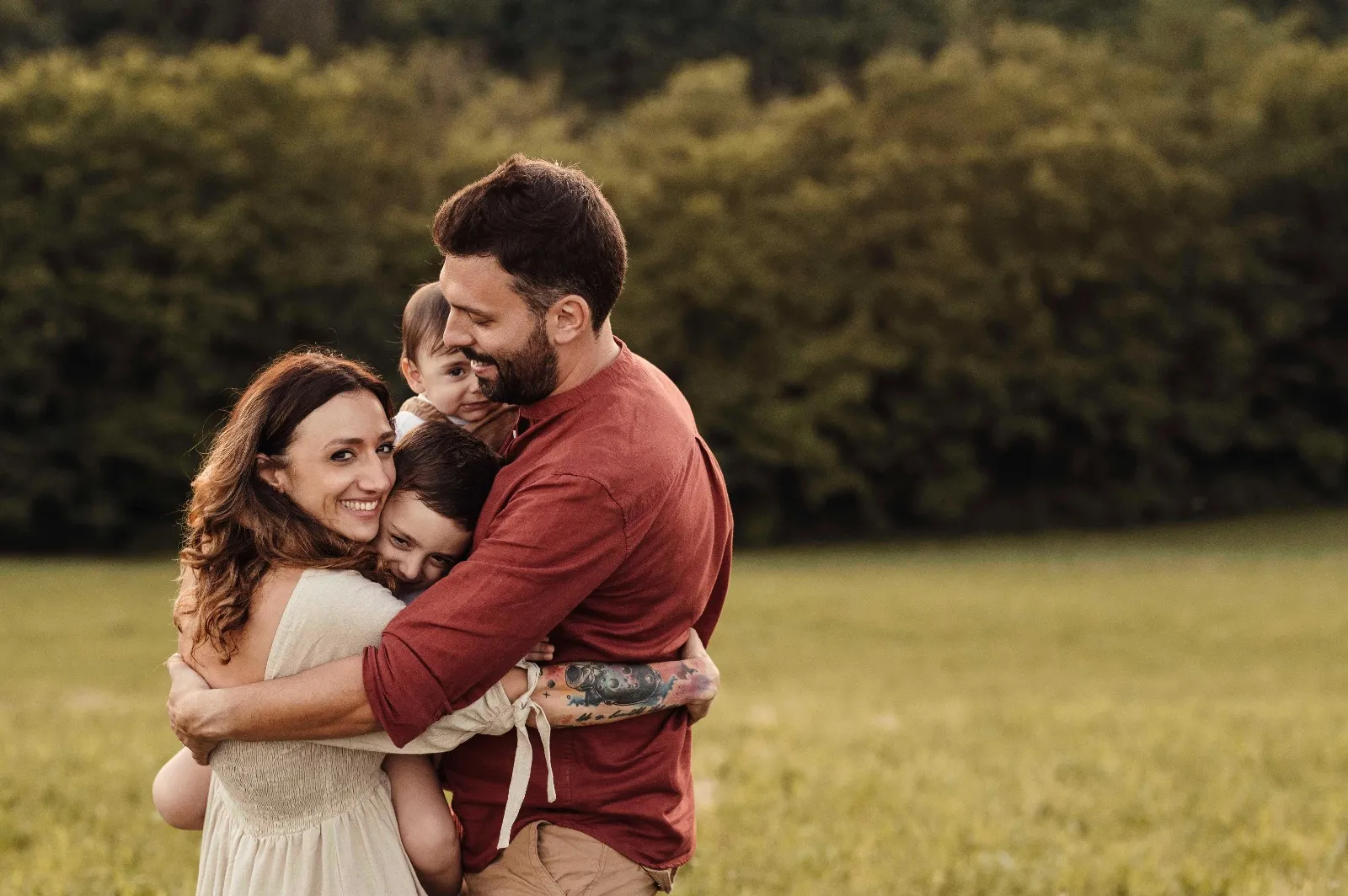 Servizio fotografico di famiglia in esterna: mamma, papà e due bambini stretti in un abbraccio in un prato
