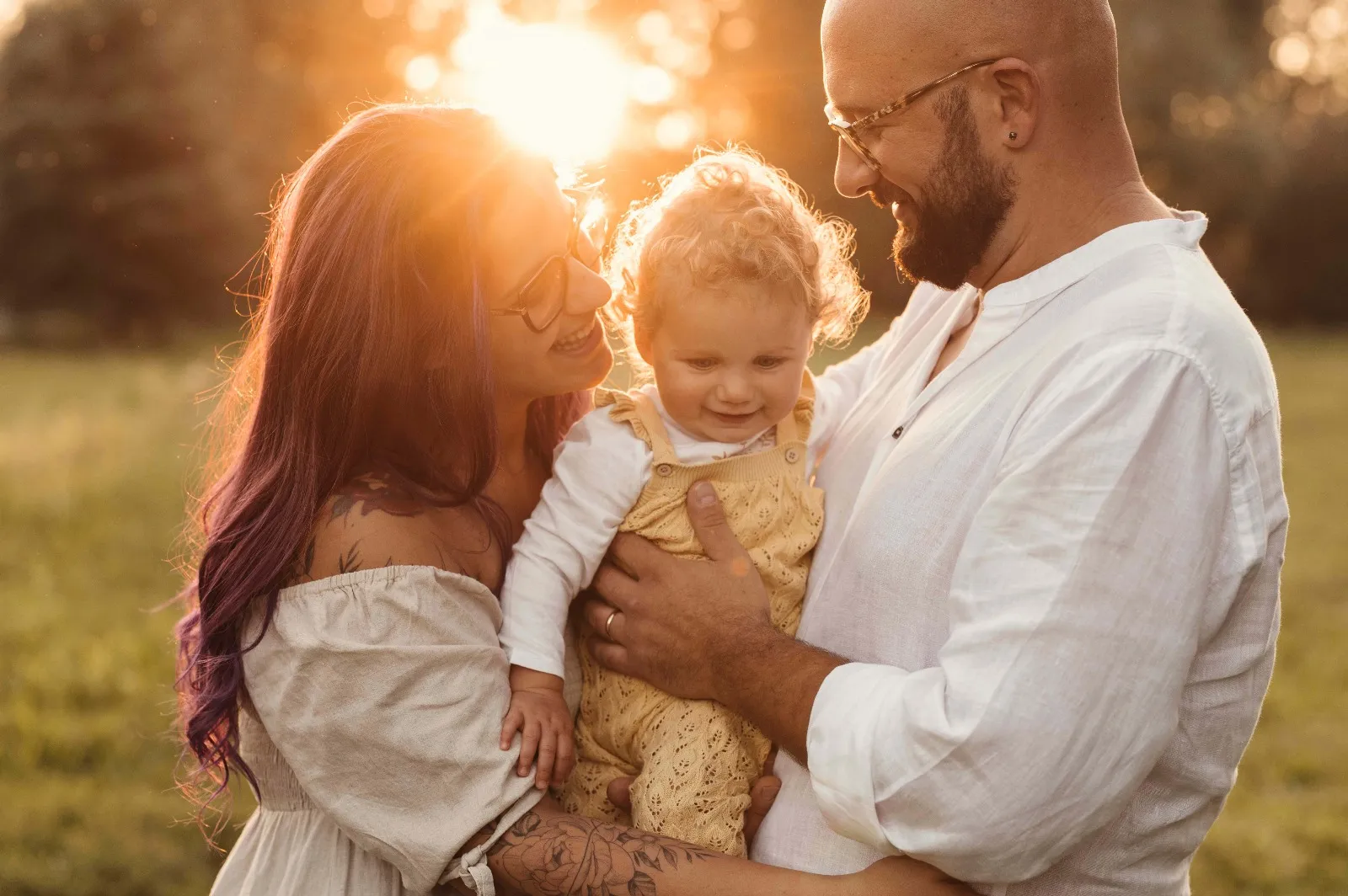 Sessione famiglia al tramonto: mamma e papà con la bimba in braccio, in controluce