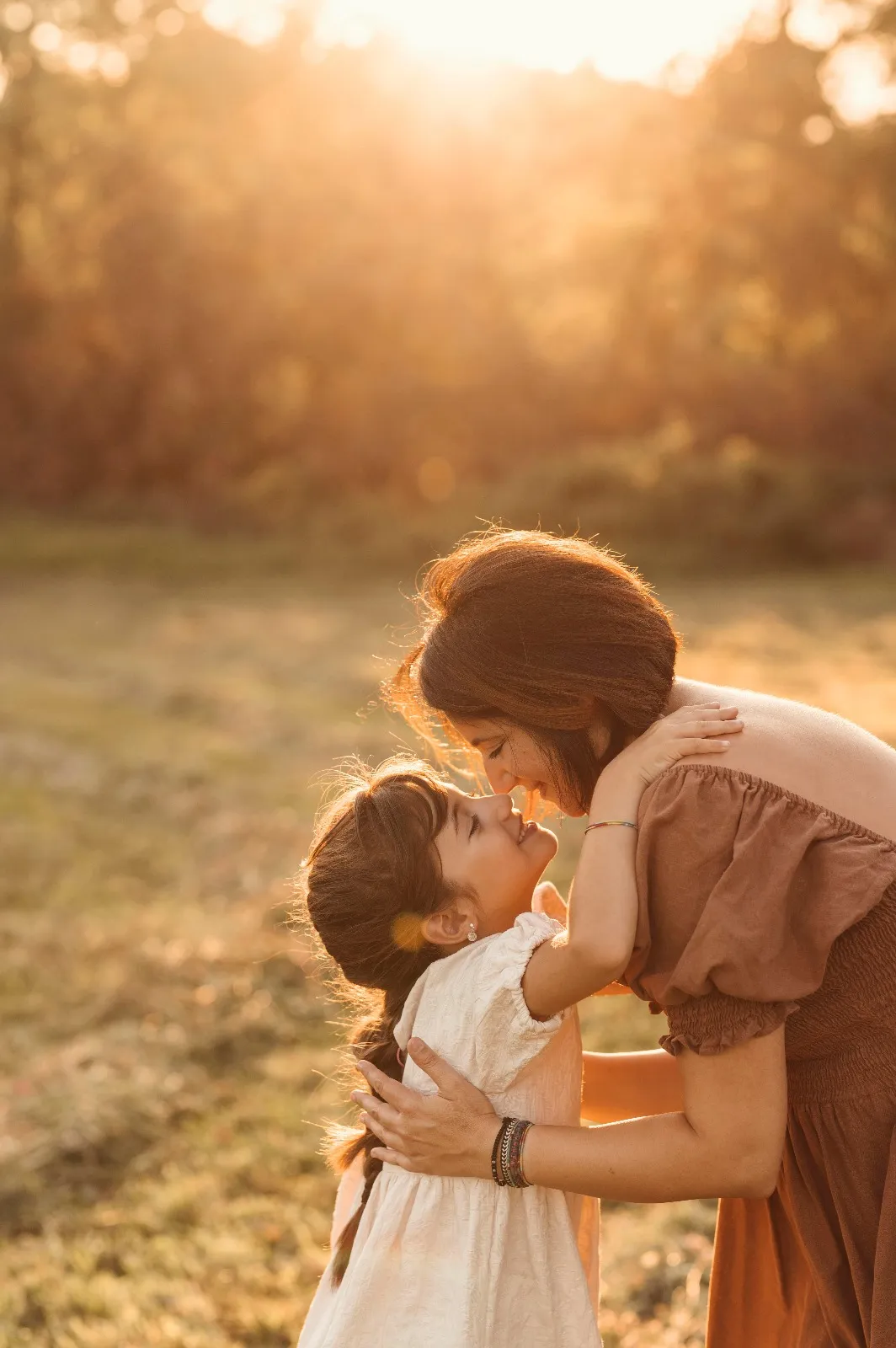 Sessione famiglia al tramonto: mamma e figlia naso a naso in controluce in un prato