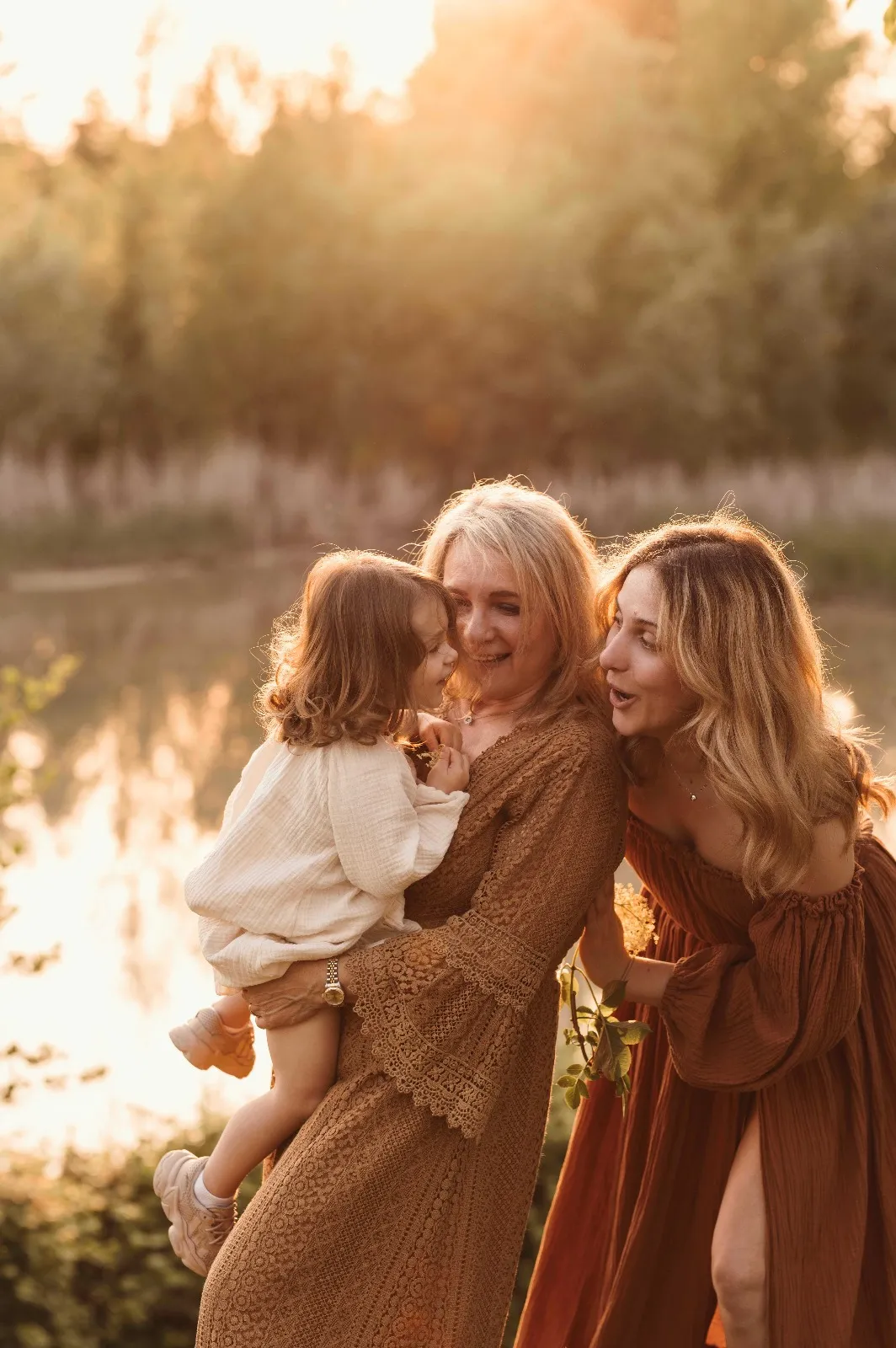Servizio fotografico di famiglia al tramonto: due donne e una bambina in riva a un laghetto, luce dorata