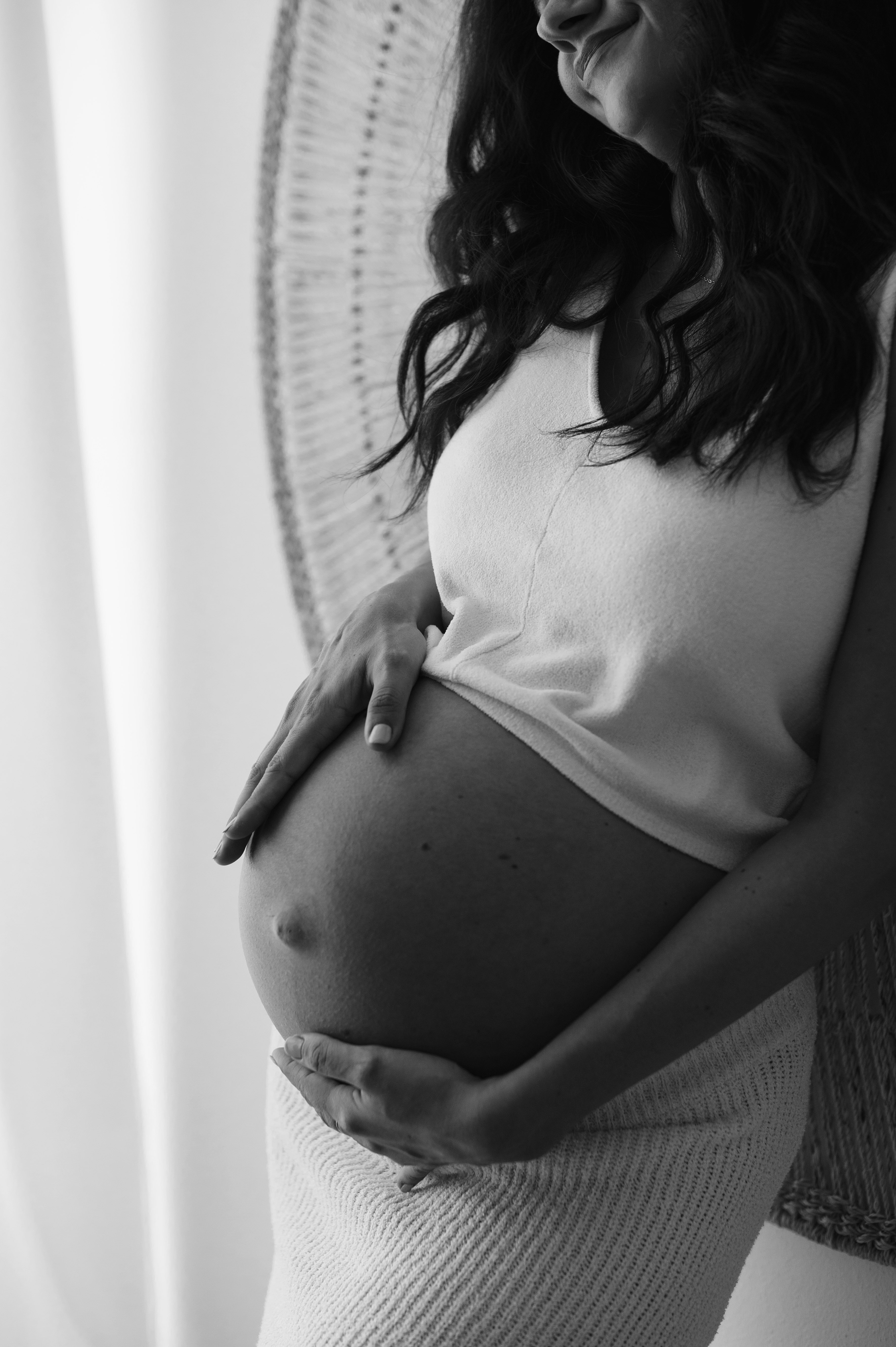 Servizio fotografico gravidanza in studio: dettaglio del pancione con le mani della mamma, luce naturale, in bianco e nero