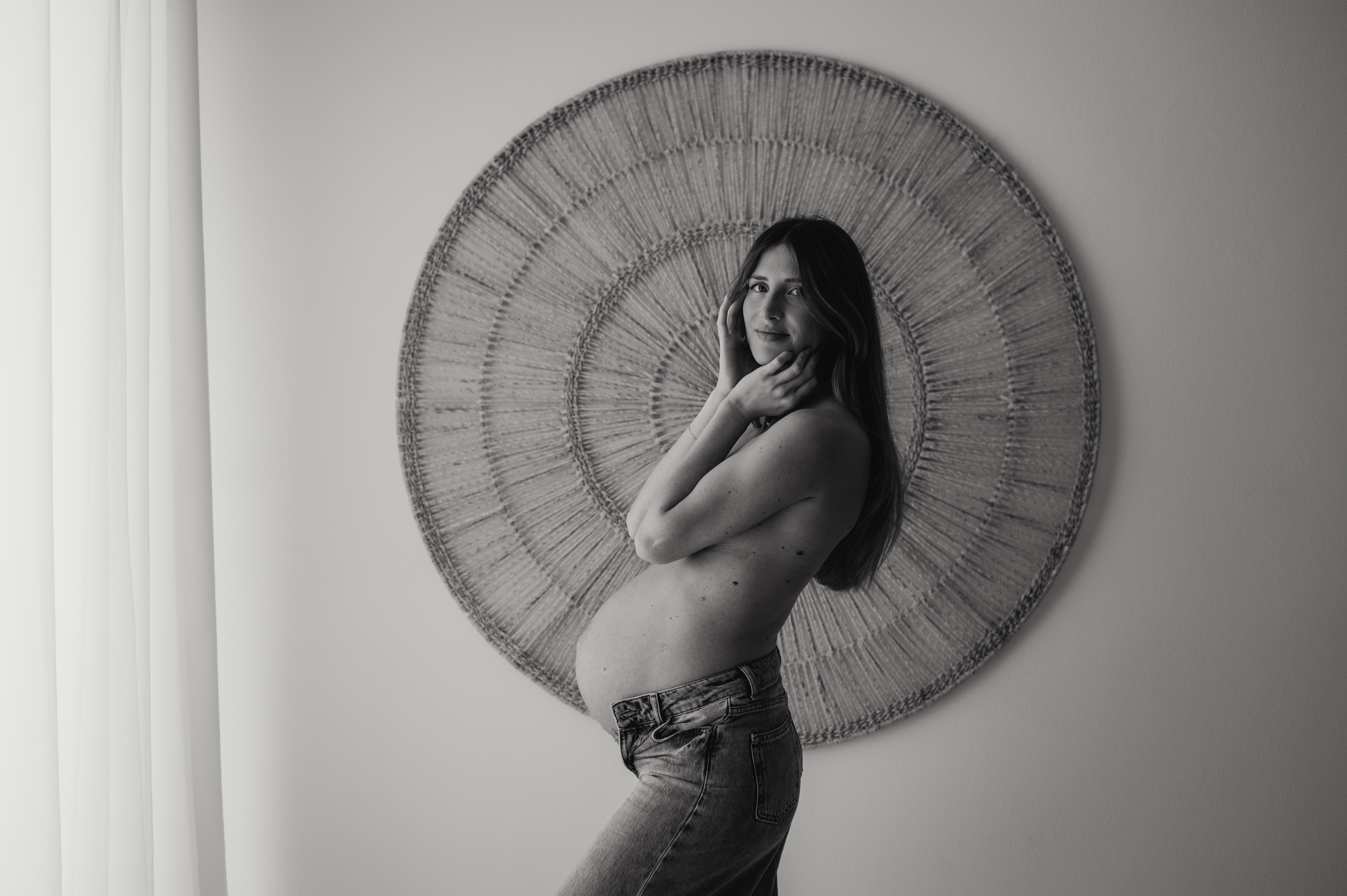 Servizio fotografico gravidanza in studio: ritratto della futura mamma in jeans davanti a un arazzo circolare, in bianco e nero